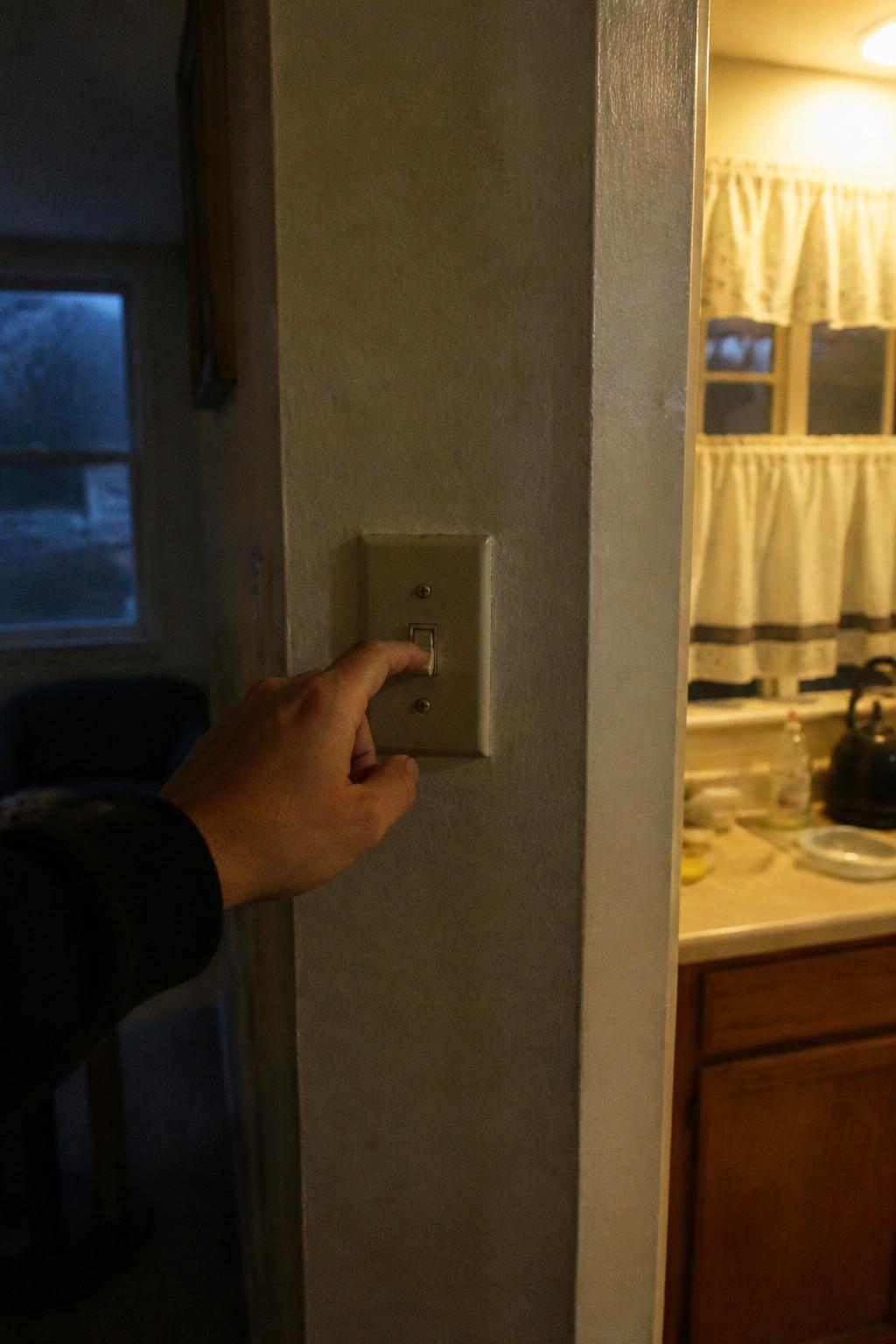 A hand turning on a kitchen light switch at dusk